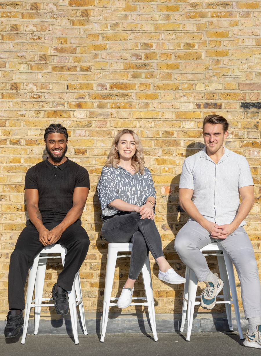 Marketing team sitting on stools against a brick wall and smiling